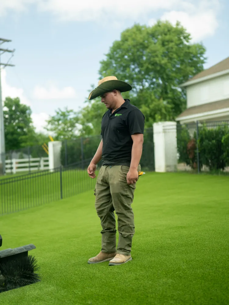Worker inspecting green artificial grass during a commercial turf installation project