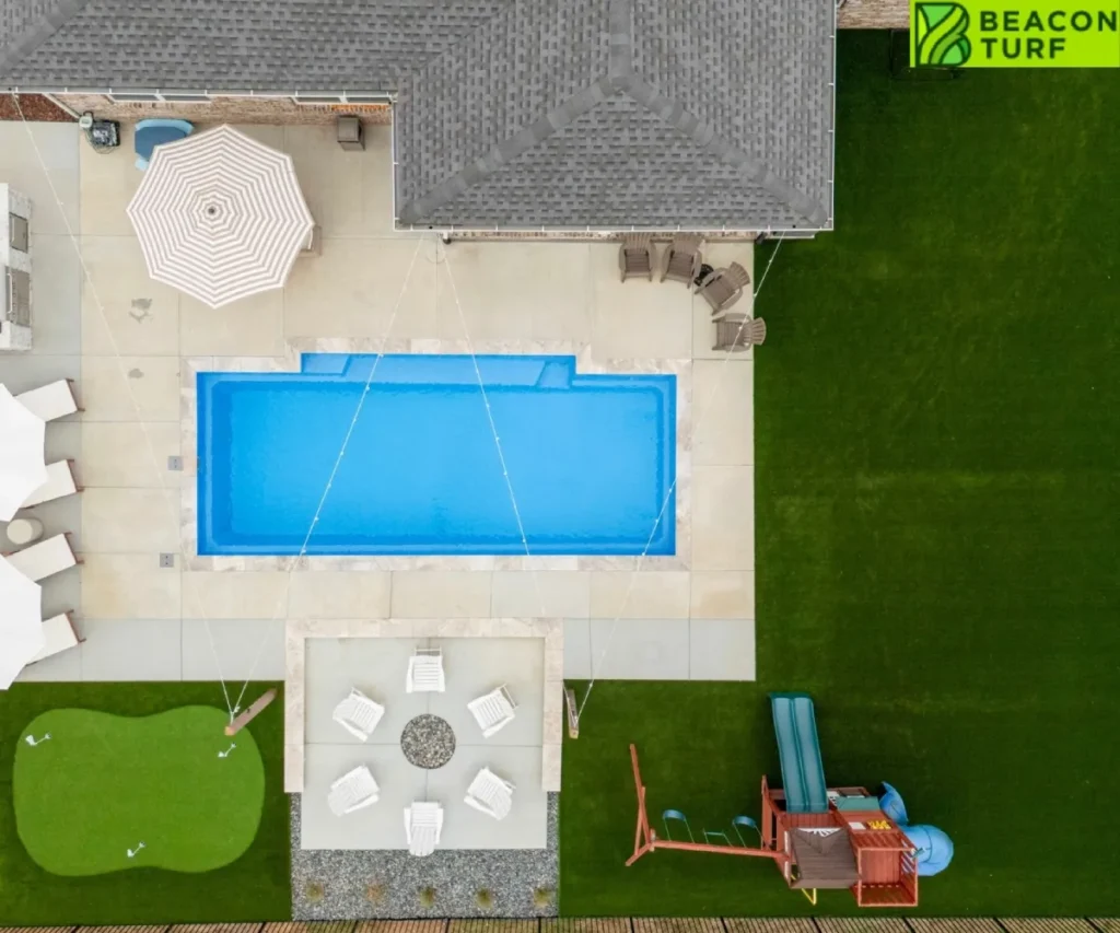 Overhead aerial view of a backyard featuring a swimming pool, fire pit lounge, putting green, children's playset, and artificial turf lawn.