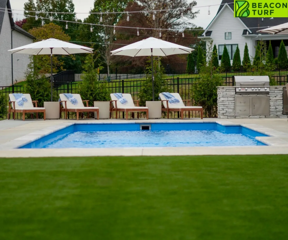 Swimming pool with lounge chairs and white umbrellas surrounded by a vibrant green artificial turf lawn in a backyard.